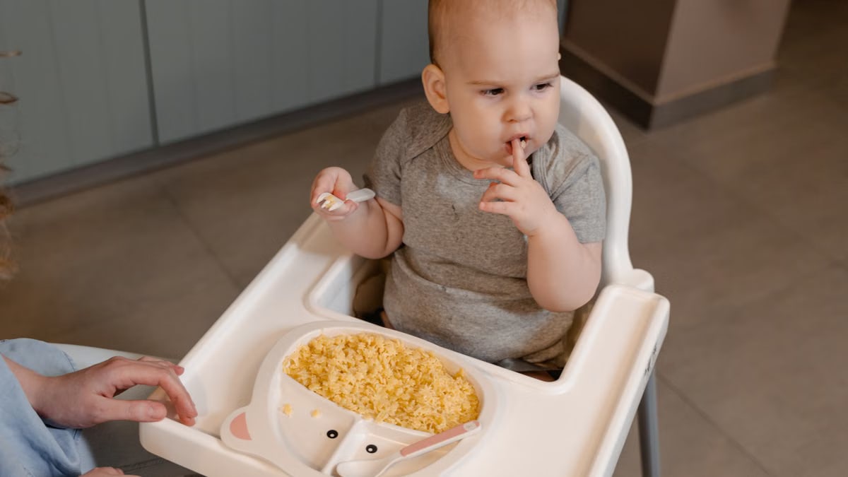 A cute baby sits in a high chair enjoying a meal indoors.
